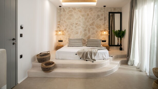 Une chambre moderne avec un mur en pierre, une lucarne, un lit avec deux oreillers, des lampes de chevet et une plante en pot.