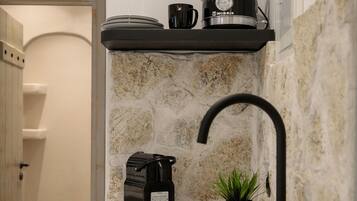 Une cuisine équipée d’un évier, d’une machine à café, d’une bouilloire et d’une plante en pot.