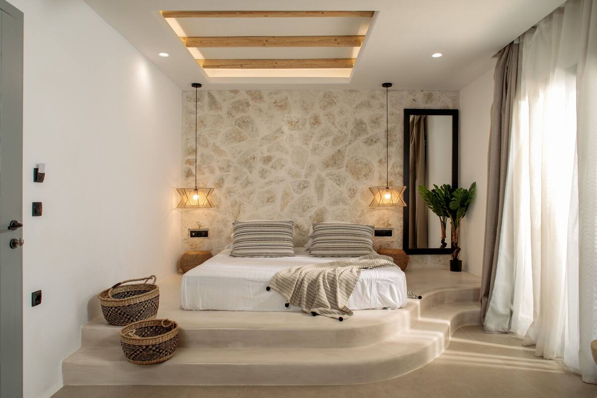 A bedroom with a bed, two bedside tables, a large mirror, a potted plant, and a staircase leading to another level.