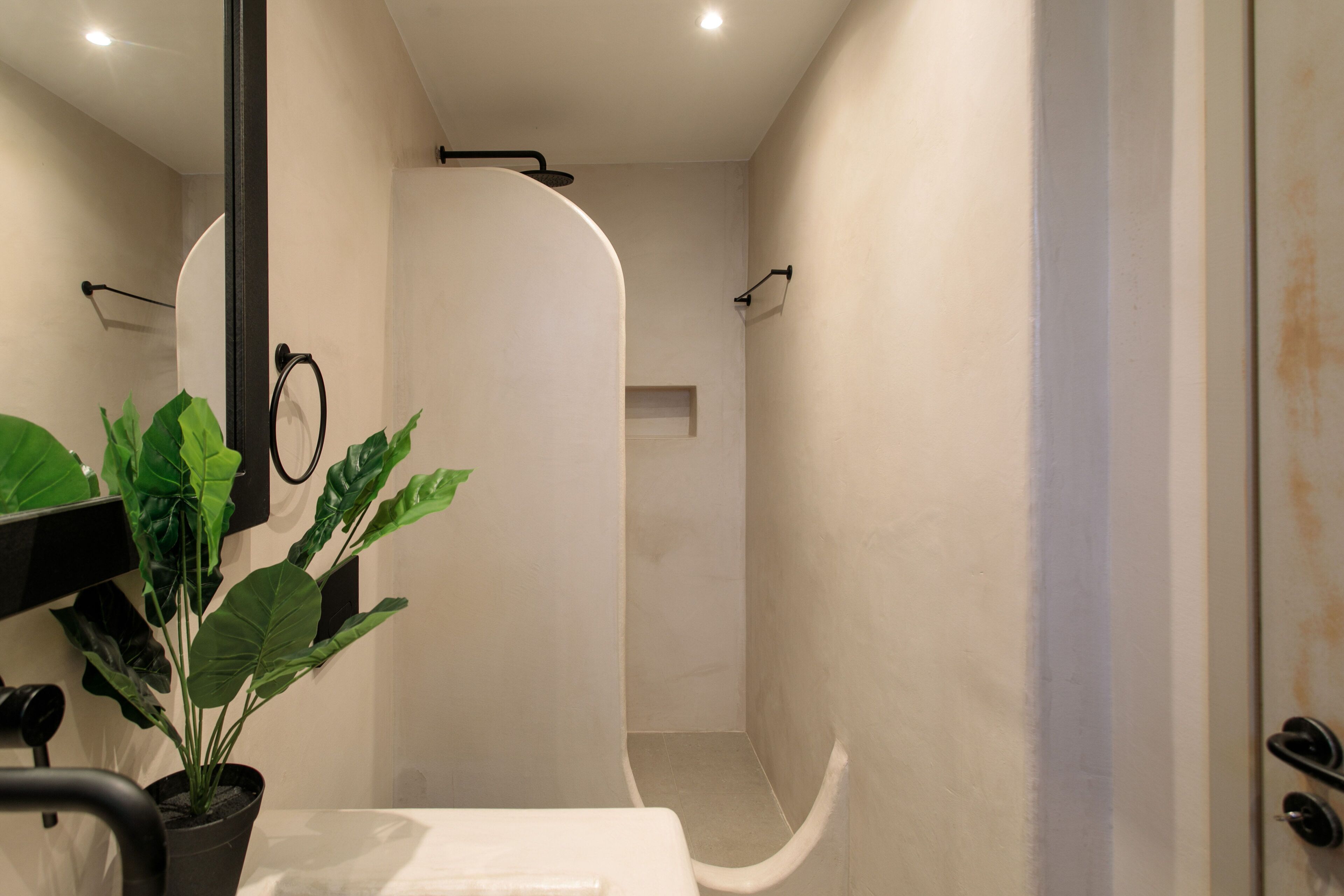 Un baño con ducha, inodoro y lavamanos. Hay una planta en maceta cerca del lavamanos.