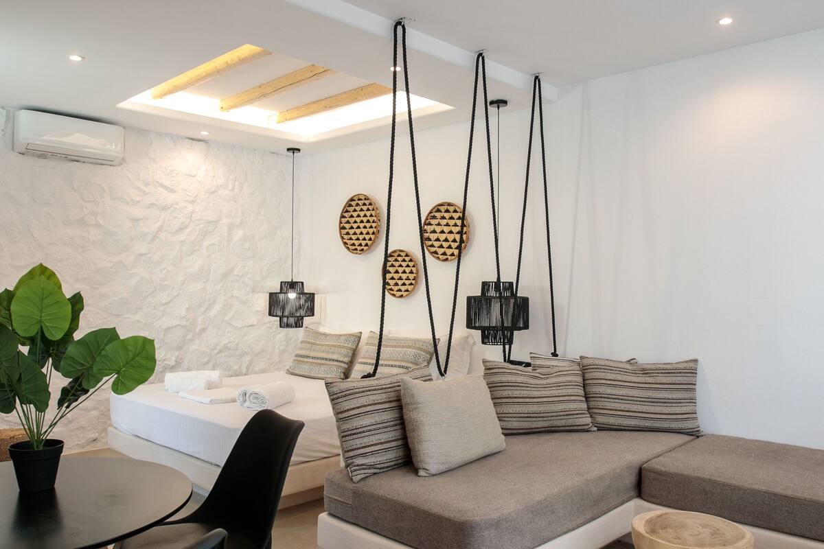 A modern living room with a sectional sofa, a dining table with chairs, and a hanging light fixture.