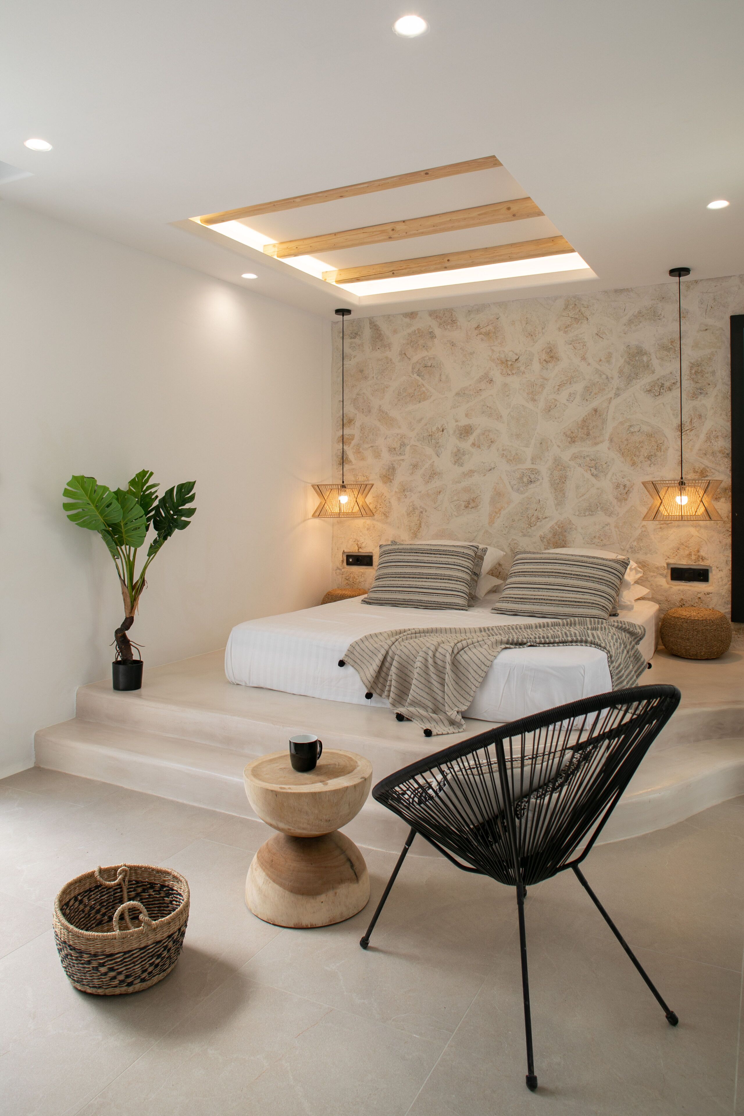 A modern bedroom with a bed, bedside lamps, a potted plant, a chair, and a small wooden table.
