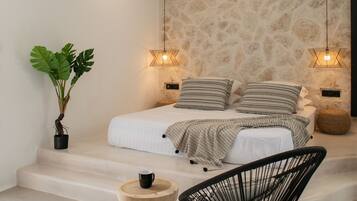 A modern bedroom with a bed, bedside lamps, a potted plant, a chair, and a small wooden table.