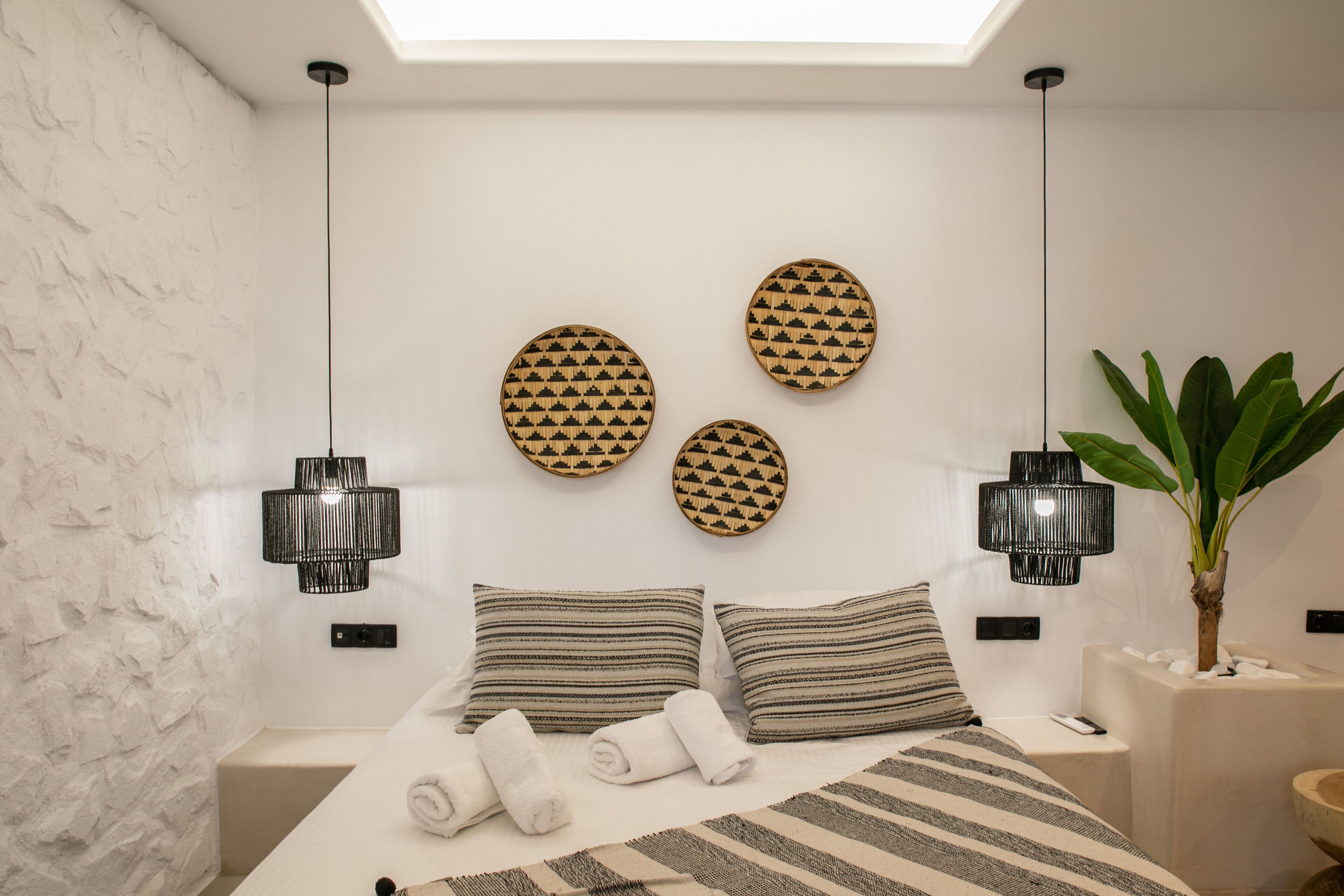 A modern bedroom with a skylight, a bed with striped bedding, two wall-mounted lamps, and a potted plant.