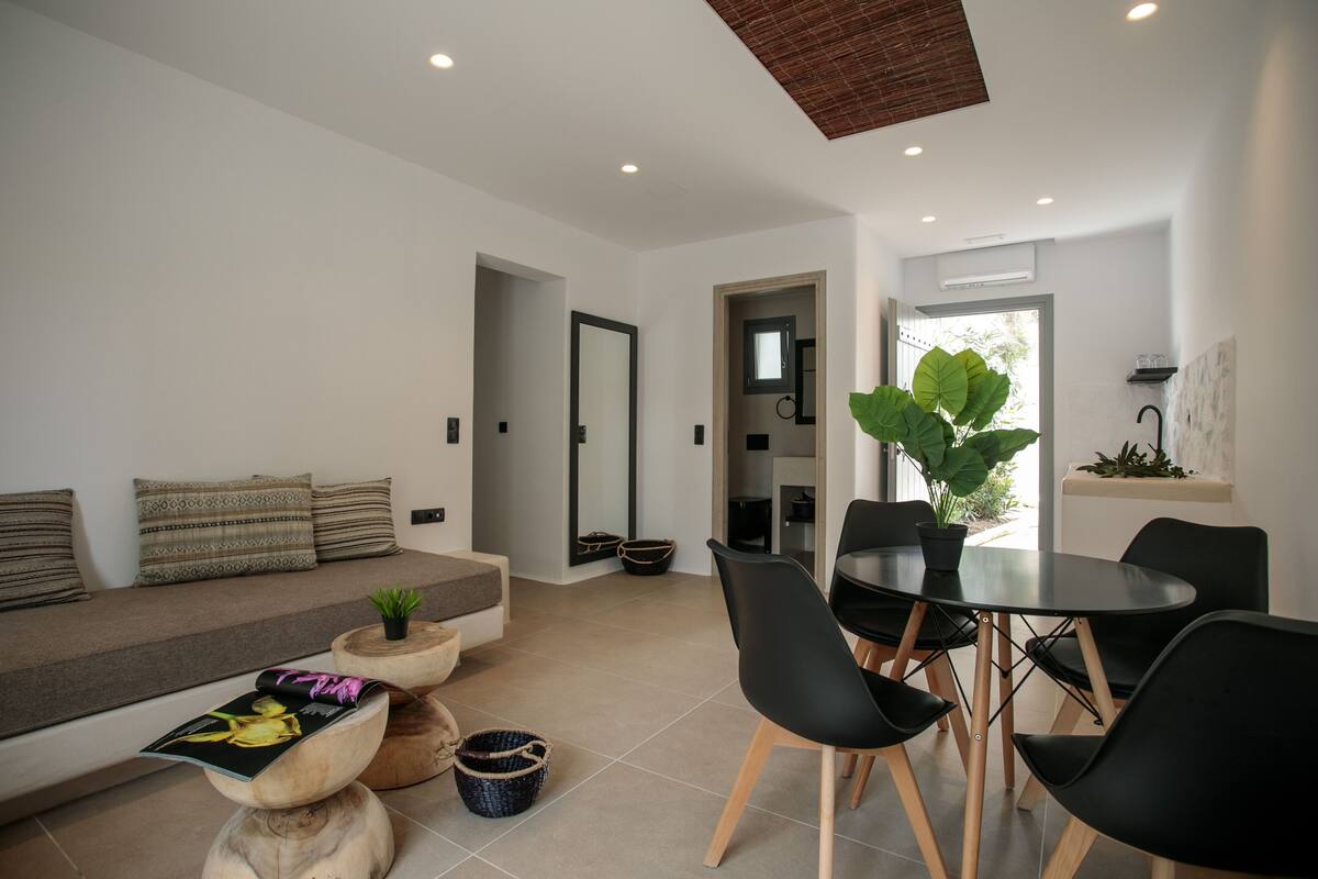 A modern living room with a sofa, dining table, chairs, and a large plant.