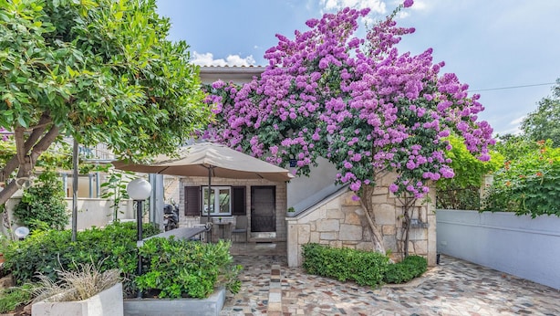 A courtyard with a stone wall, a tiled floor, and a pergola with purple flowers. - 2 bedroom beautiful apartment in Premantura (Premantura)