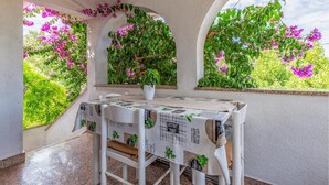 A table set for two with a tablecloth featuring a bistro theme, positioned under a window with a view of lush greenery and purple flowers. - 2 bedroom beautiful apartment in Premantura (Premantura)