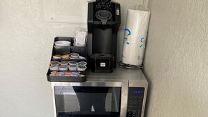 Una kitchenette compacta con microondas, cafetera y un cesto de basura.