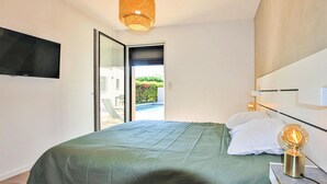 Een slaapkamer met een bed, een aan de muur bevestigde televisie en uitzicht op een buitenzwembad.