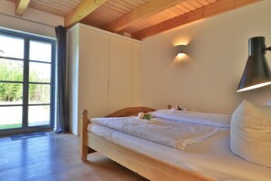 Een slaapkamer met een houten bed, een raam met gordijnen, een wandlamp en uitzicht op groen.