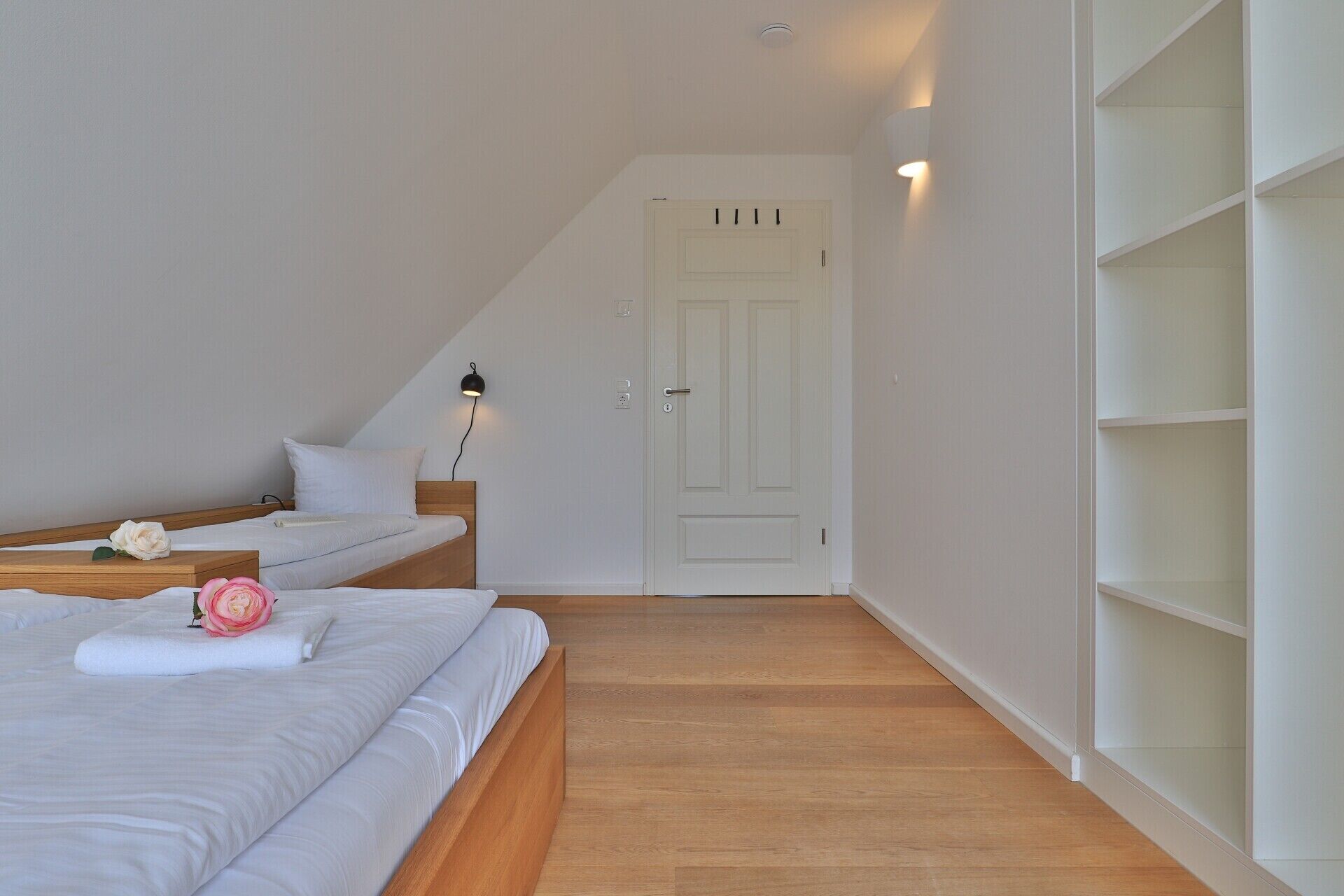 Une chambre à coucher avec un lit, une table de chevet, une lampe fixée au mur et une porte blanche.