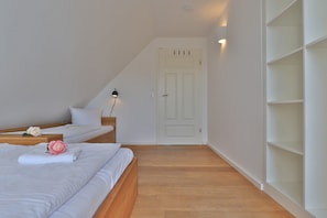 Une chambre à coucher avec un lit, une table de chevet, une lampe fixée au mur et une porte blanche.