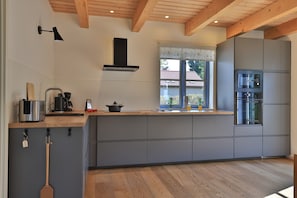 Een moderne keuken met grijze kastjes, een houten aanrecht, een inbouwoven en een raam met uitzicht op een huis.
