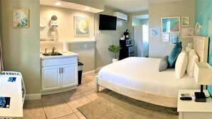 A hotel room with a bed, a desk with two photos, a sink, a microwave, and a TV. - Quaint Queen Deluxe (Daytona Beach)