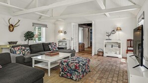 A spacious living room with a white ceiling, grey sofas, a white coffee table, and a floral ottoman. A deer skull hangs on the wall, and there is a fireplace with a lamp. - 3 bedroom cozy home in Hals (Hals)