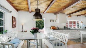 A kitchen with white cabinets, a dining table with white chairs, and a hanging light fixture. - 3 bedroom cozy home in Hals (Hals)
