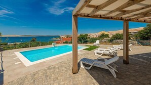 Una piscina con lettini e un pergolato affacciata su un paesaggio costiero.