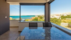 Un balcone con tavolo e sedie in vetro, vista sulla costa, case e cielo sereno.