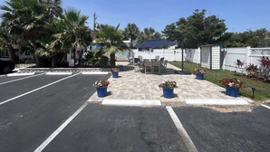 A parking lot with a patio area featuring a table and chairs, surrounded by potted plants and a white fence. - Restful Queen Deluxe (Daytona Beach)