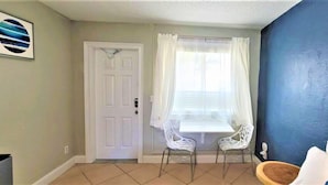 A room with a white door, a window with white curtains, two white chairs, and a blue wall. - Restful Queen Deluxe (Daytona Beach)