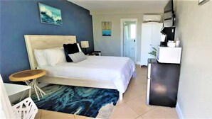 A hotel room with a bed, a small table, a desk, a microwave, and a wardrobe. - Restful Queen Deluxe (Daytona Beach)