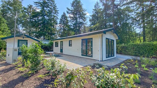 Une cabane à deux étages dotée d’un patio couvert et d’un petit jardin.