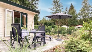 Une terrasse extérieure avec une table et des chaises, entourée de verdure et avec une petite maison en arrière-plan.