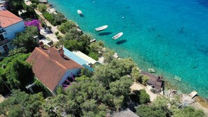 Ein Luftbild einer Küstenlandschaft mit klarem türkisblauem Wasser, Booten und Gebäuden mit roten Ziegeldächern.