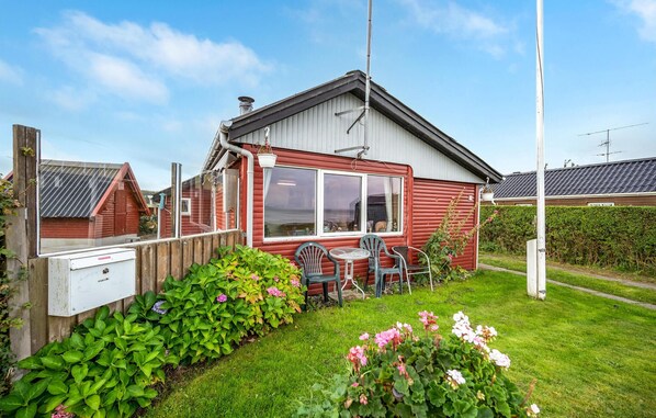 Une maison mobile rouge avec un petit jardin, une clôture en bois et une antenne parabolique.