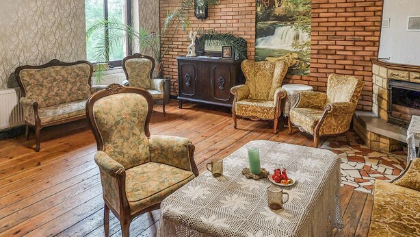 A cozy living room with wooden flooring, floral-patterned furniture, a fireplace, and a large window.