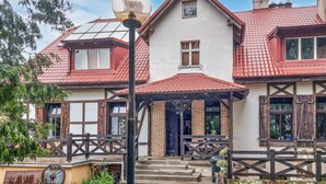 A traditional two-story house with a red-tiled roof, a wooden porch, and a black lamp post.