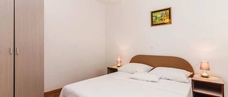 A bedroom with a bed, bedside lamps, a wardrobe, and a painting on the wall.