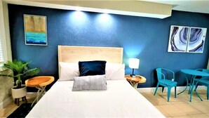 A hotel room with a large bed, a nightstand, a lamp, a potted plant, and a seating area with chairs.
