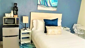 A bedroom with a bed, a nightstand, a microwave, a refrigerator, a painting, and a chair. - Zesty Queen Deluxe (Daytona Beach)