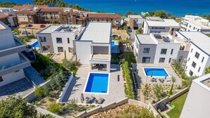Et boligområde med moderne bygninger, en swimmingpool og udsigt til havet.