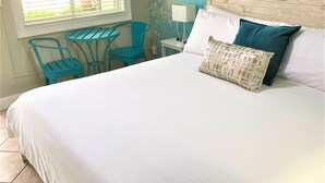 A bedroom with a large bed, a small table, two chairs, a lamp, and a wall mural. - Tranquil King Deluxe (Daytona Beach)