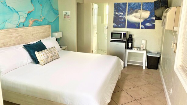 A hotel room with a large bed, a desk with a microwave, a coffee maker, and a trash bin. - Tranquil King Deluxe (Daytona Beach)