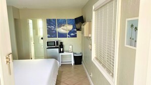 A hotel room with a bed, a small table with a microwave, a coffee maker, and a trash bin. There are two paintings on the wall, one of a shark and one of a palm tree. - Tranquil King Deluxe (Daytona Beach)