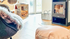 A modern living room with a fireplace, a wicker basket with firewood, and a grey armchair. - Awesome apartment in Büsum with sauna (Büsum)