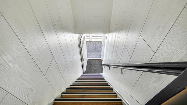 Una escalera con paredes blancas y escalones de madera que conduce a un espacio exterior.
