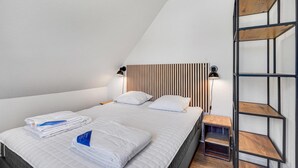 Un dormitorio moderno con techo inclinado, cama con ropa de cama blanca, dos lámparas de noche y cabecero de madera.