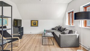 Un loft moderno con cama alta, un sofá gris, una mesita de centro pequeña y un televisor sobre un mueble bajo.
