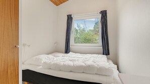 Een kleine kamer met een enkel bed, een raam, witte muren en een houten plafond.