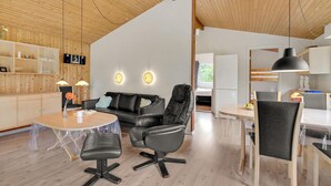 Een modern interieur met een houten plafond, een leren zwarte bank, een eettafel en een keukenhoek.