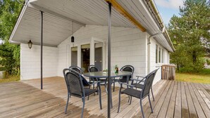 Een overdekt terras met een ronde tafel, vier stoelen, een vuilnisbak en een raam.