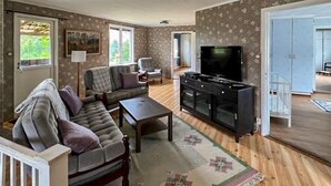 A living room with a sofa, a coffee table, a TV, and a cabinet. There are windows and a door visible. - Nice home in Rörvik with WiFi (Rörvik)