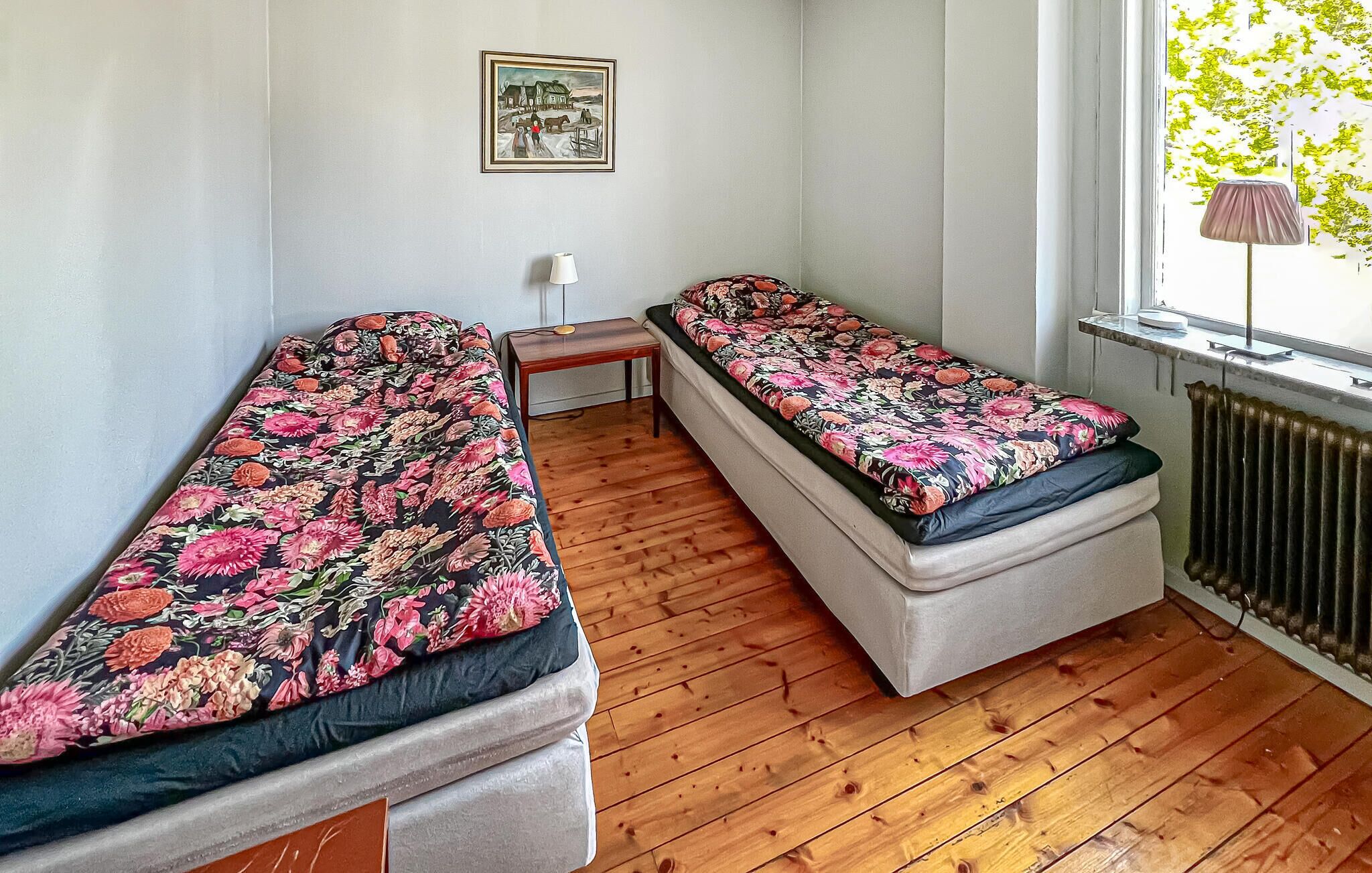 Une chambre avec deux lits simples, une petite table, une lampe et un radiateur.
