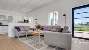 A modern living room with a grey sofa, a wooden coffee table, and a view of the outdoors through large windows. - 2 bedroom amazing home in Rødby (Rødby)