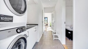 A laundry room with two front-loading washing machines, a tiled floor, and a view into a dining area through an open door. - 2 bedroom amazing home in Rødby (Rødby)