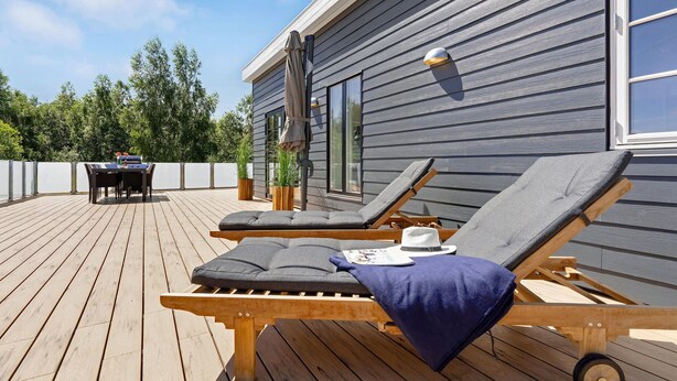 A wooden deck with two sun loungers, a table, and chairs. - 2 bedroom amazing home in Rødby (Rødby)